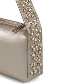 Bolso de mano metálico dorado con una textura suave, que cuenta con un cierre con cremallera y una correa adornada con tachuelas redondas transparentes.