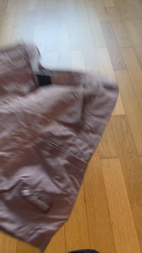 Light brown wrinkled pants laid on a wooden floor, partially folded with a visible black waistband inside.