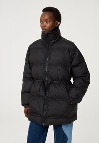 Zwarte pufferjack met hoge kraag, getailleerde taille en een zigzagsteekpatroon. Met fleece gevoerde zakken en ritsafsluiting.