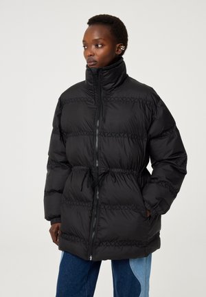 Zwarte pufferjack met hoge kraag, getailleerde taille en een zigzagsteekpatroon. Met fleece gevoerde zakken en ritsafsluiting.