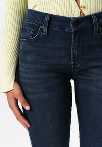 Tumedast sinine denim, millel on sobiv disain, tavalised taskud, nupuga sulgemine ja õrn tekstuurimuutus kangal.