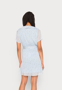 Vestido floral azul con mangas cortas transparentes, cintura entallada y dobladillo con volantes. Presenta un sutil patrón de margaritas y un cuello con solapa.