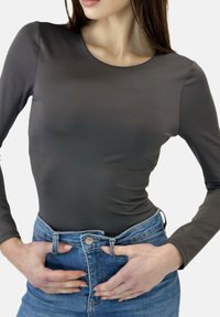 Grijs langärmelig romper van gladde stof, gecombineerd met een high-waist blauwe spijkerbroek met knoopsluiting en voorzakken.