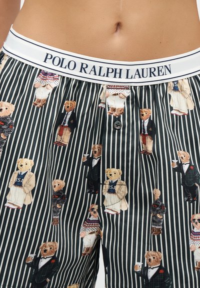 Taille et bas du torse portant un short Polo Ralph Lauren à rayures foncées avec divers ours en peluche vêtus de tenues formelles et décontractées imprimés sur le tissu.
