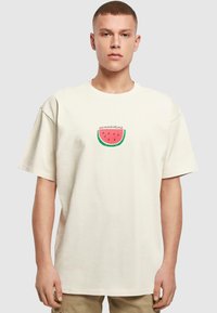 Beige bomulds t-shirt med korte ærmer og løs pasform. Har et rundt grafik af en vandmelon med teksten "sommertid" i et legende skrifttype.