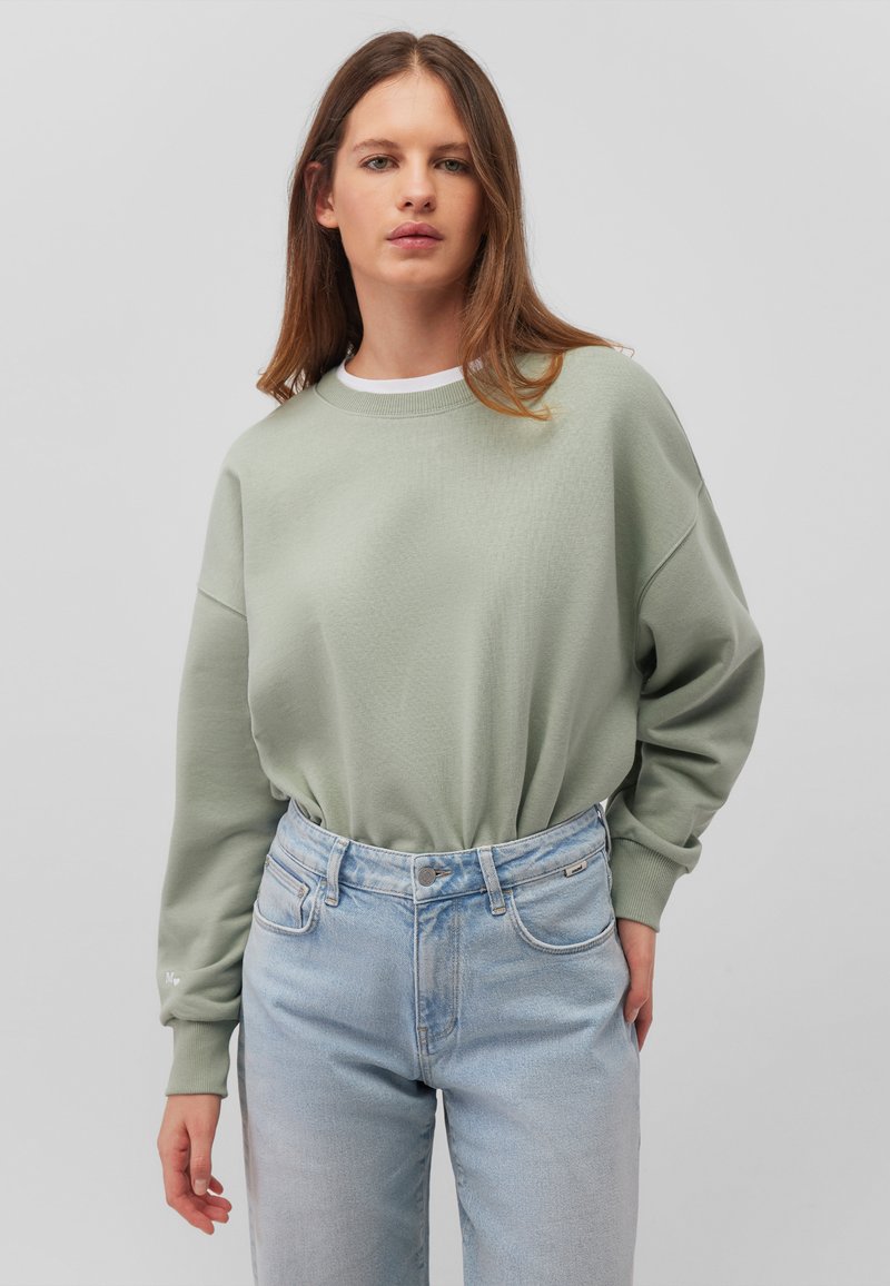 Felpa oversized verde menta con finitura texture e collo a coste, abbinata a jeans azzurri a vita alta.