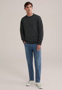 Sweatshirt de culoare gri închis, cu guler rotund și manșete ribbate, asortat cu blugi drepti de culoare albastră deschisă și adidași albi cu accente colorate subtile.