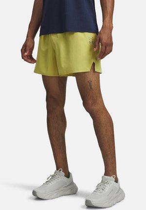 Yellow athletic shorts with side slits, logo detail, and breathable fabric, paired with white sneakers featuring a gray accent.