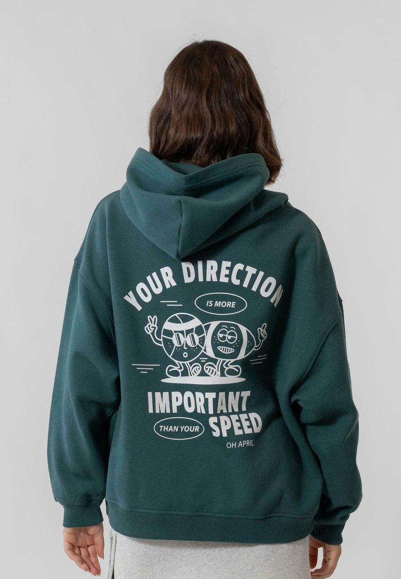 Zöld kapucnis pulóver, nagy grafikai mintával a hátsó részen, amely játékos karaktereket és a következő szöveget tartalmazza: "A TE IRÁNYOD FONTOSABB, MINT A SEBESSÉGED."