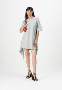 Gray short-sleeve dress with asymmetric hem, made of soft fabric. Paired with black strappy heels and a small red handbag.