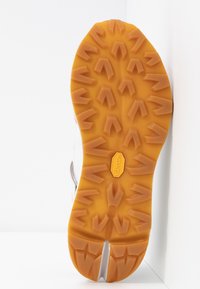 Semelle d'une chaussure de randonnée avec des crampons profonds et anguleux en caoutchouc orange, logo Vibram au centre.