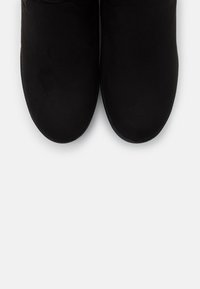 Bottes noires en daim jusqu'à la cheville avec un bout rond et un design minimal, dotées d'une semelle plate et d'une texture douce, vues de dessus.