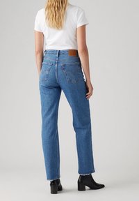 Vaqueros de mezclilla azul con corte recto, cintura alta y un leve desgastado. Presentan bolsillos traseros y un parche de cuero marrón en la cintura.