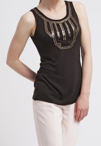 Zwarte mouwloze top met een beadontwerp over de borst en een aansluitende snit, gecombineerd met lichte, rechte broek.