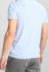 Camiseta de rayas azul claro con mangas cortas, de material de algodón, cuello redondo y un diseño ajustado. Detalles de costura visibles en los hombros.