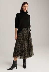 Maglione nero a collo alto con dettagli in oro abbinato a una lunga gonna trasparente a stampa leopardata e stivali neri a punta.