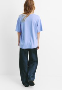 Tricou oversized de culoare violet deschis, cu mâneci scurte, asociat cu blugi evazați de culoare albastru închis. Material texturat, potrivire casual.