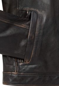 Details van een bruine leren jas met een zichtbare zak, die de gestructureerde oppervlakte en gestikte accenten benadrukt, en de natuurlijke afwerking van het materiaal toont.