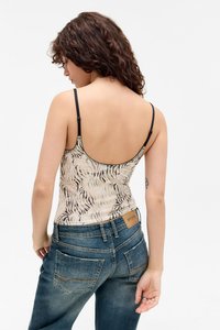 top in cotone aderente con un motivo a strisce di tigre beige e nero; spalline nere; indossato con jeans in denim blu con tasche posteriori.