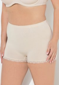 Pantaloni corti in cotone beige con una texture liscia. Presentano un delicato pizzo lungo l'orlo e un tessuto elasticizzato per comfort e vestibilità.