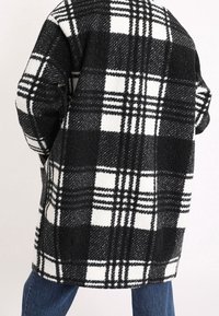 Cappotto a quadri bianco e nero, realizzato in tessuto morbido, con grandi motivi a scacchi, vestibilità oversize e spalle scese.