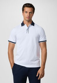 Biely polo tričko s námorníckym golierom a lemovaním, so skratkou na gombíky. Vyrobené z hladkej tkaniny, so subtilnými detailmi loga.