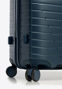 Valigia rigida blu navy con righe orizzontali, doppie ruote girevoli, chiusura a zip e maniglie rinforzate per una facile manovrabilità.