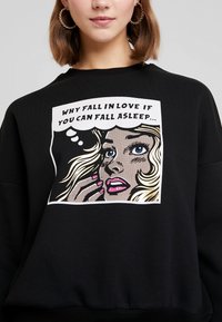 Felpa nera con un grafico di cartone che presenta il volto di una donna, labbra colorate e la scritta: "PERCHÉ INNAMORARSI SE PUOI ADDORMENTARTI..."