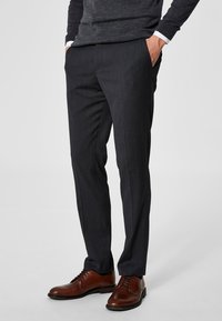 Mørk grå skreddersydde bukser med en glatt tekstur, rett snitt og subtile stripemønster. Brukt med brune lærskjorter.