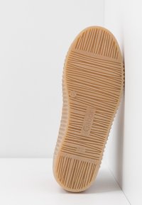 Podeszwa brązowego kauczukowego buta z liniowym wzorem bieżnika, z nazwą marki "Gabor" wytłoczoną na środku, spoczywająca na białych powierzchniach.