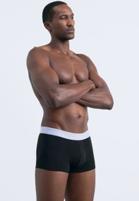 Fekete boxer alsónadrág fehér Calvin Klein derékszíjjal, sima anyagból készült, testhezálló kialakítással és függőleges varrással az elején.