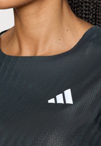 Crni sportski top s okruglim izrezom, teksturiranim materijalom s suptilnim uzorcima i bijelim adidas logotipom s lijeve strane.