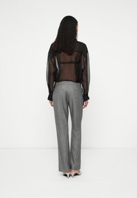 Μαύρο �διάφανο μπλουζάκι με μακριά μανίκια, σε συνδυασμό με ανοιχτό γκρι παντελόνι με καρό σχέδιο και γκρι τακούνια, από πίσω όψη.