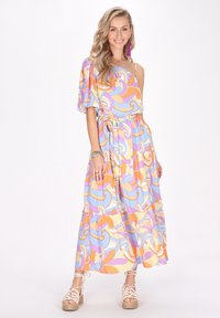 Maxikleid mit einem Schulterträger in Pastellfarben, das mit gewundenen Mustern, elastischem Taillenbund und Rüschen am Saum versehen ist. Kombiniert mit geflochtenen Espadrilles.