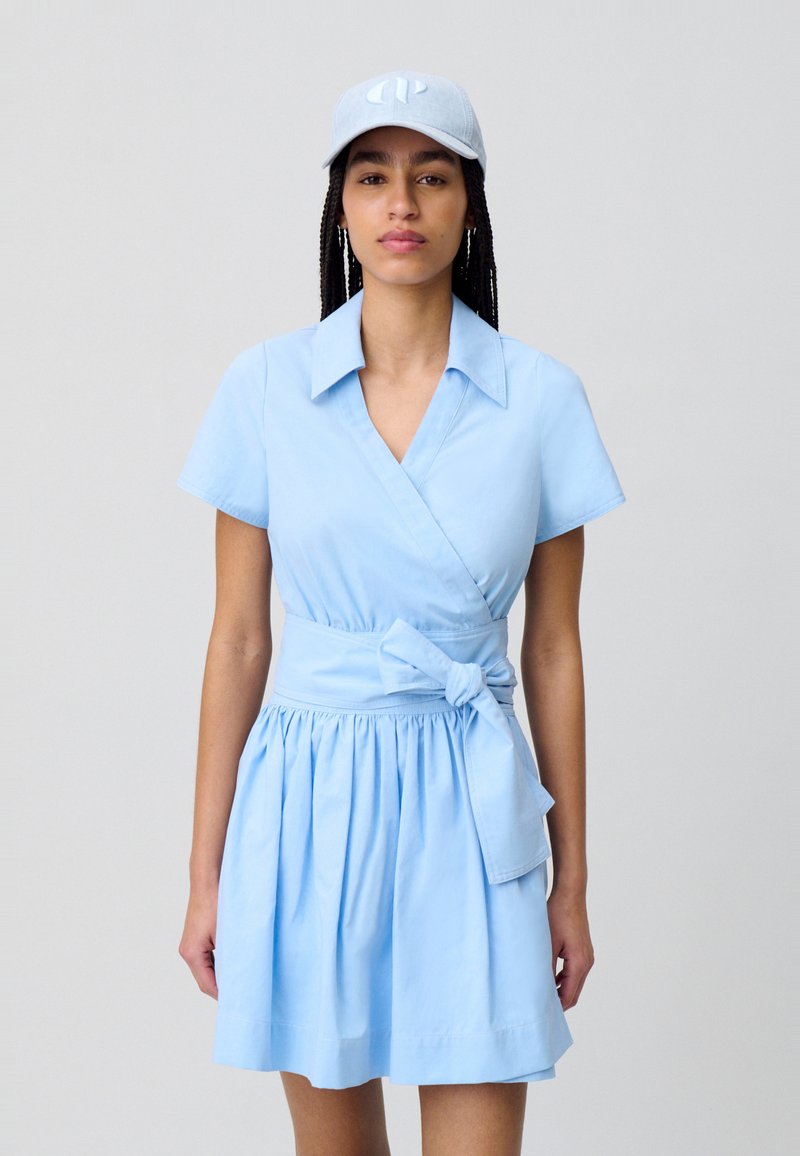 Robe portefeuille bleu clair en mélange de coton avec des manches courtes, une ceinture à nouer à la taille et une jupe évasée ; assortie d'une casquette correspondante.