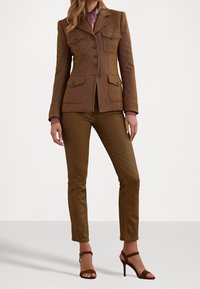 Brun tweedblazer med knäppning och två framfickor, kombinerad med skräddarsydda bruna byxor och bruna högklackade sandaler med remmar.