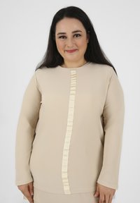 Maglietta a maniche lunghe beige con dettaglio in nastro verticale testurizzato di una tonalità più chiara, con scollatura rotonda e tessuto morbido.