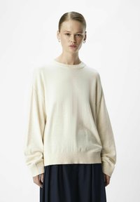 Cremefarvet sweater med en afslappet pasform, ribbet halsudskæring og lange ærmer; parret med en navy nederdel, som har en glat tekstur og minimal dekoration.