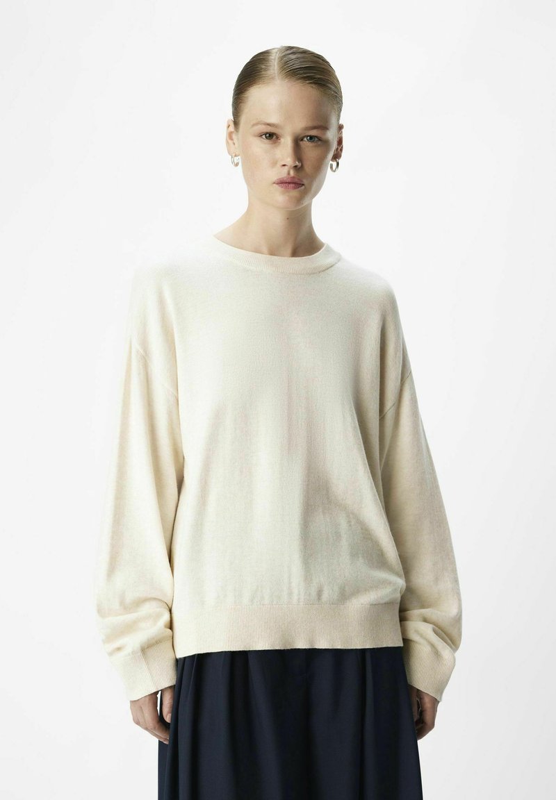Cremefarvet sweater med en afslappet pasform, ribbet halsudskæring og lange ærmer; parret med en navy nederdel, som har en glat tekstur og minimal dekoration.