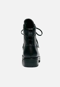 Botas ankle de cuero negro con un acabado texturizado, punta redonda y tacón cuadrado. Presentan cordones y una cremallera lateral para facilitar su uso.