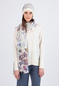 Floral-patterned scarf and beanie in cream, featuring purple, pink, and yellow accents. Soft knit texture, designed for warmth. Model wearing casual sweater and pants.