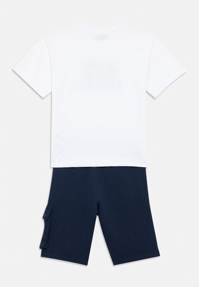 Λευκό βαμβακερό μπλουζάκι με κοντά μανίκια, συνδυασμένο με σορτς σε ναυτικό μπλε χρώμα που διαθέτει τσέπη cargo στο πλευρό, και τα δύο παρουσιασμένα μαζί.