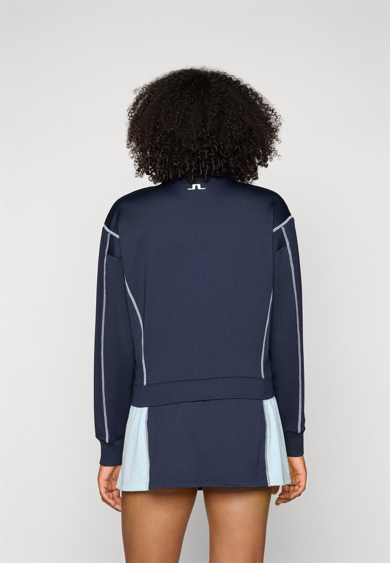 Navy athletic sweatshirt featuring gray stitching and a logo on the collar. The bottom hem has a fitted design above a light blue skirt.