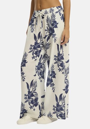 Pantaloni leggeri a gamba larga con un motivo floreale blu navy, indossati con sneakers bianche. La vita presenta un cordino per la regolazione.