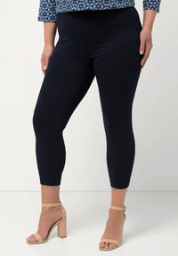 Marinblå caprileggings i stretchtyg, med en slät yta och resårmidja, tillsammans med beige klacksandaler.