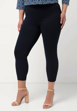 Marineblaue Capri-Leggings aus elastischem Material, mit glatter Textur und elastischem Bund, kombiniert mit beigen Blockabsatzsandalen.