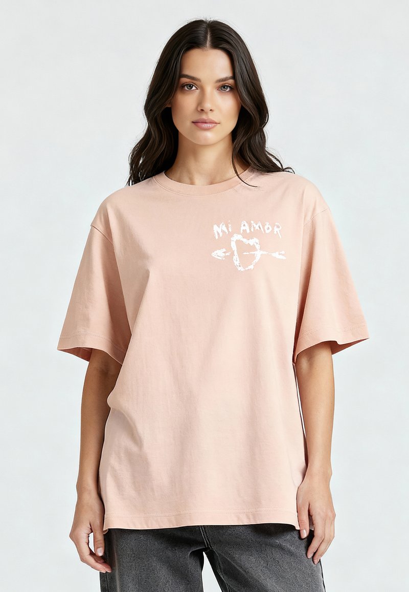 T-shirt en coton rose à coupe décontractée, présentant le texte "Mi Amor" en blanc, accompagné d'un design de cœur et de flèche sur le devant.