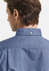 Herenblauwe chambray shirt met een button-down kraag, een soepele textuur en een geplooid achterdetail.