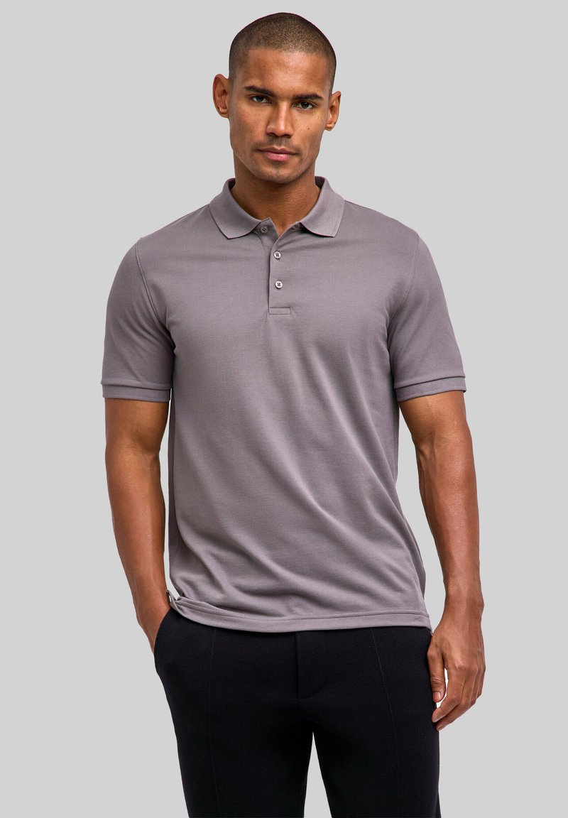 Szara koszulka polo z krótkim rękawem, kołnierzykiem i rozpinaną na trzy guziki plisą, wykonana z gładkiego materiału, noszona z czarnymi spodniami.