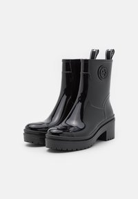 Bottines noires brillantes avec un talon épais, dotées d'un détail logo et de poignées pour un enfilage facile. Semelle en caoutchouc texturée pour une bonne adhérence.